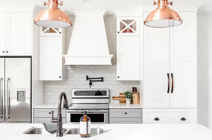 A kitchen with a white cabinet layout and copper pendant lights.