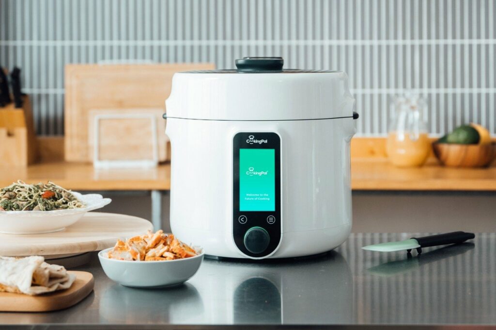 A rice cooker sits on a counter next to a bowl of food.