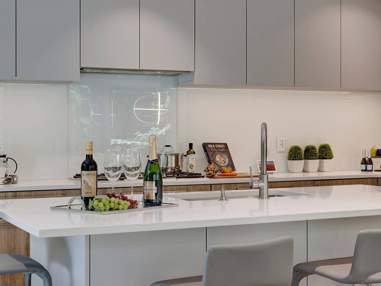 A modern kitchen with white cabinets and stools featuring sleek marble countertops.