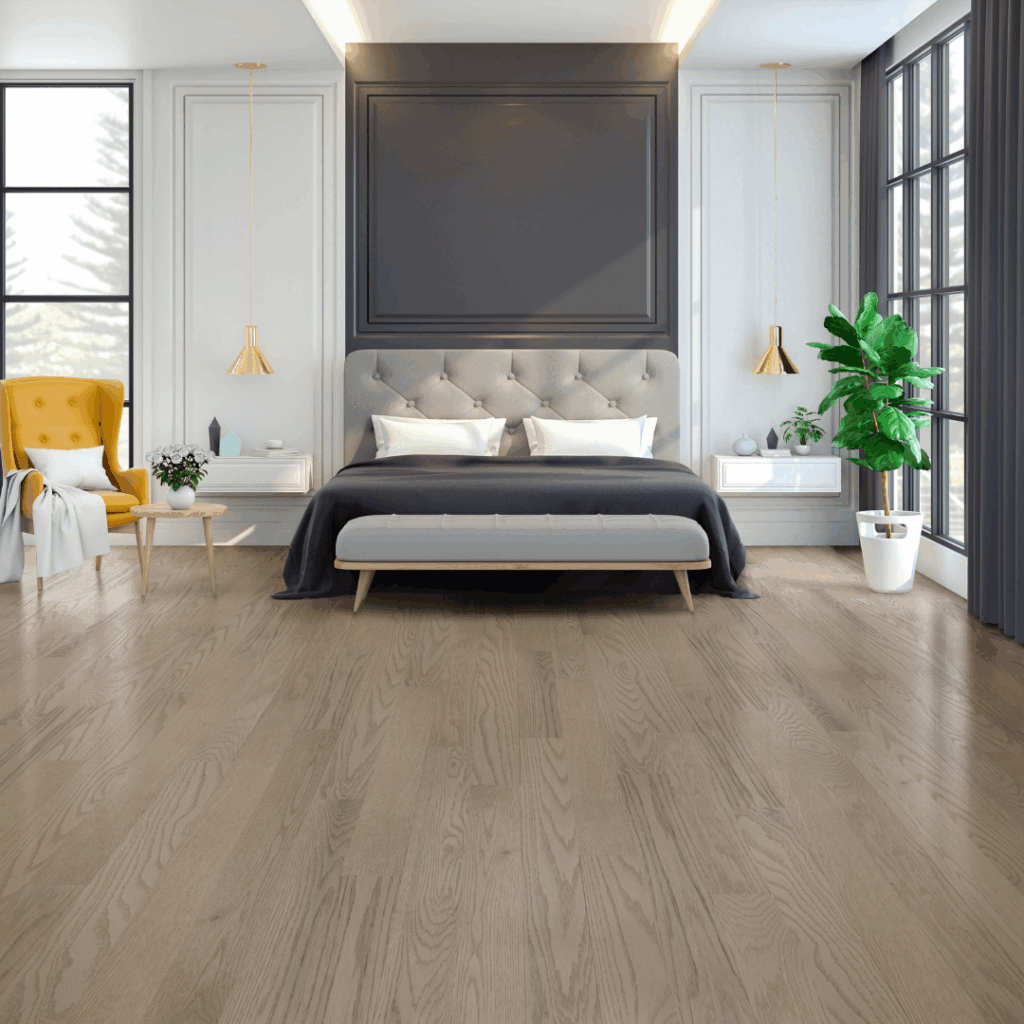 Modern bedroom with a gray tufted bed, white bedding, two pendant lights, a yellow armchair, a green potted plant, large windows, and light wood flooring.