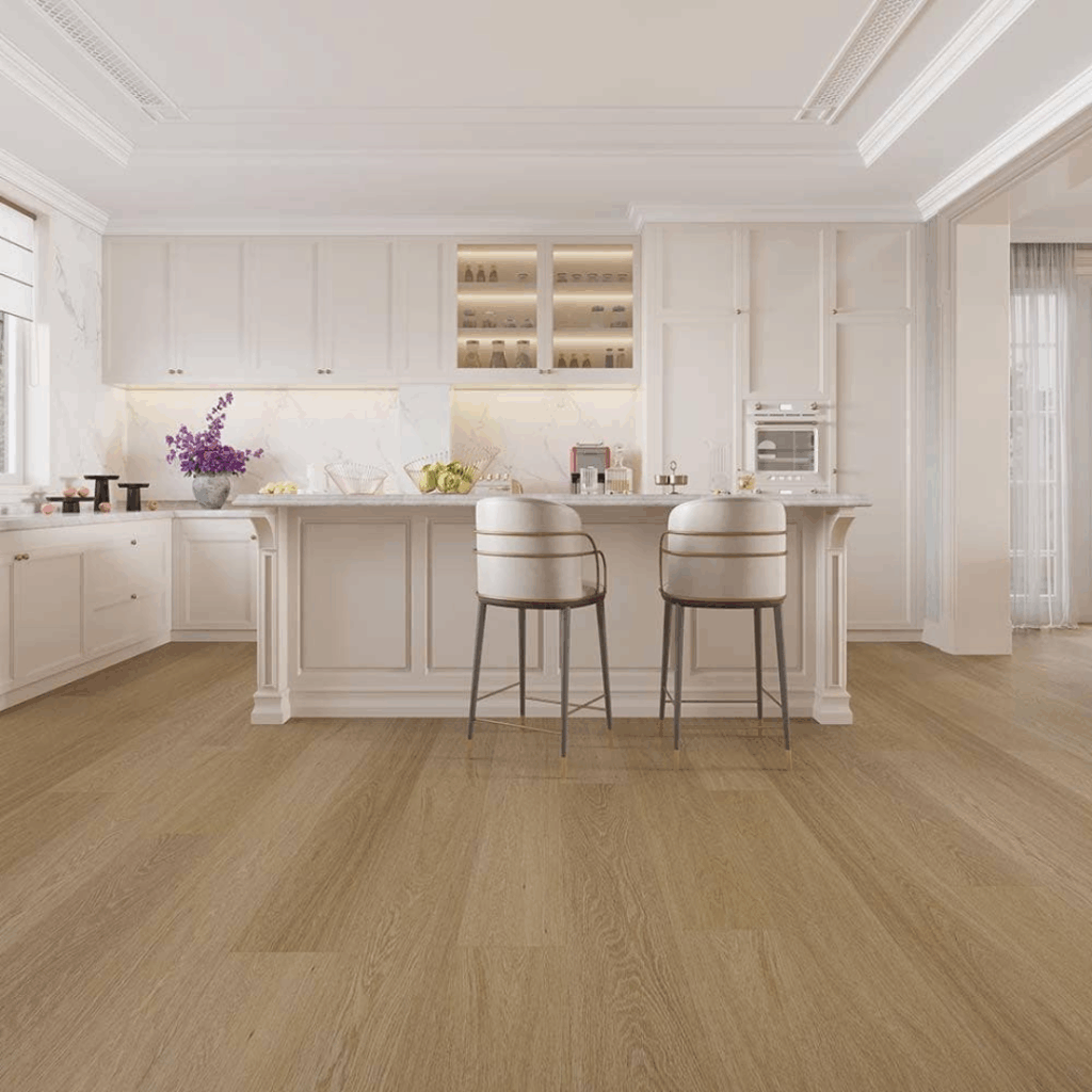Modern kitchen with white cabinets, marble countertops, a central island with two upholstered barstools, and light wood flooring. Vase with purple flowers sits on the island.