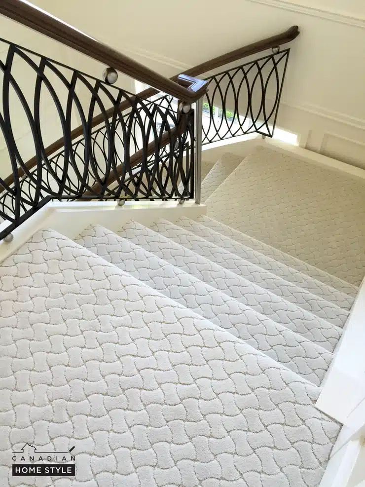A staircase with a white Stainmaster carpet and wrought iron railing.