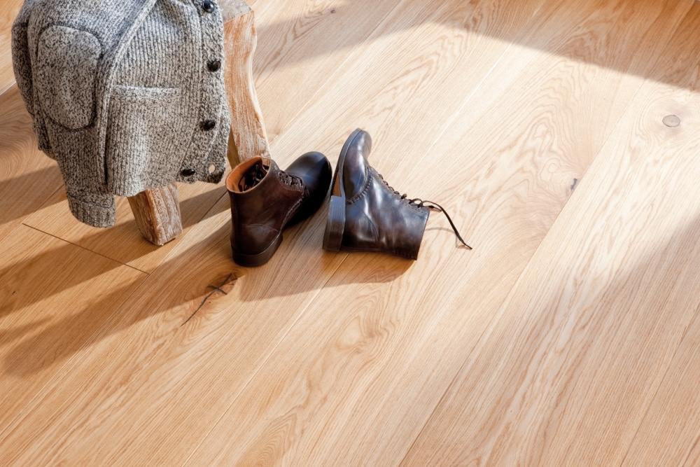 A pair of shoes and a sweater on a wide plank hardwood floor.