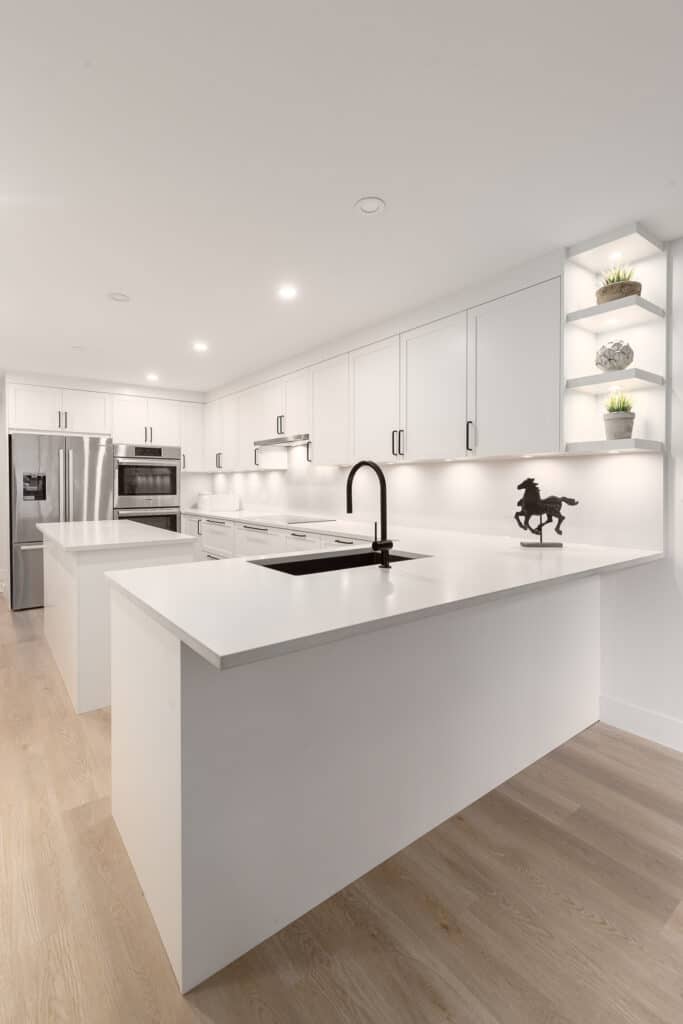 A kitchen with white cabinets and wood floors designed for Kitchen and bath design.